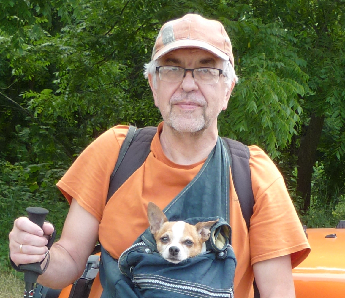 Guena outdoors wearing cap, backpack, and shoulder bag containing a chihuahua with its head popping out