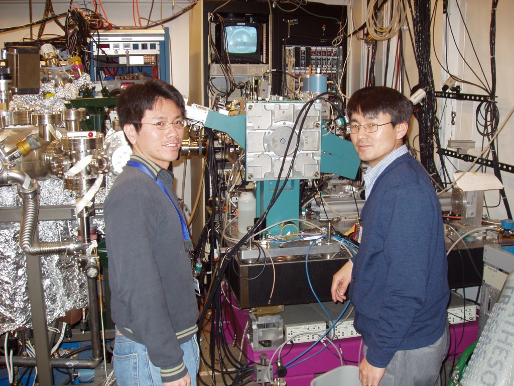 Two men in glasses and lanyards in front of an instrument with many cables and tubes everywhere